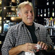 Blond man behind a bar, drying a glass